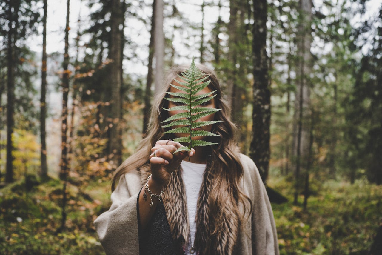 about-01 Woman holding a fern leaf in a vibrant autumn forest, capturing the beauty of nature.